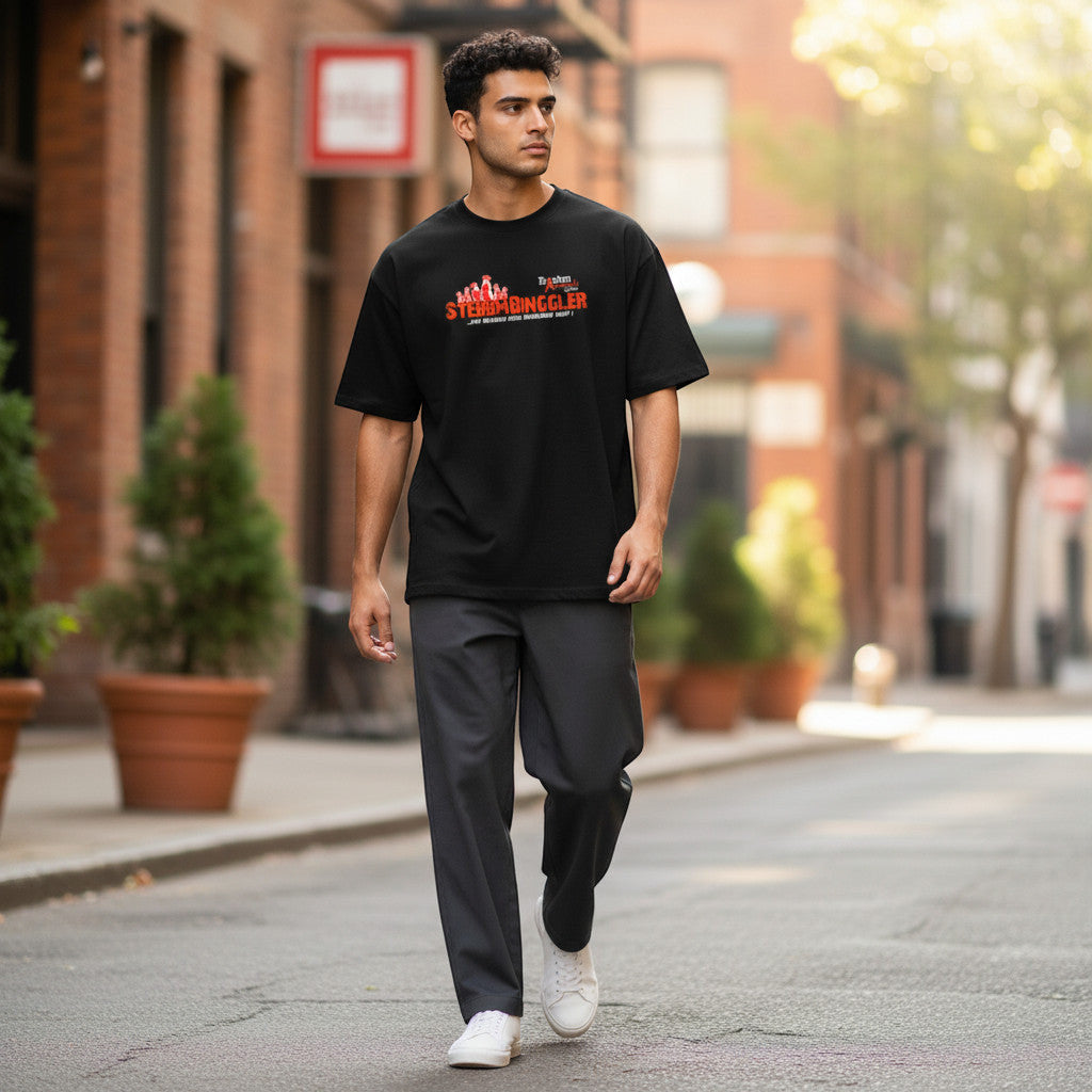 Ein Mann trägt ein schwarzes XXUwe T-Shirt mit Stebbmbinggler-Erdmännchen-Druck auf einer städtischen Straße.